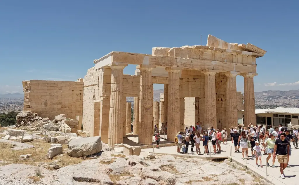 Visitors walking past the Propylaia, the marble gateway to the Acropolis, under a clear blue sky