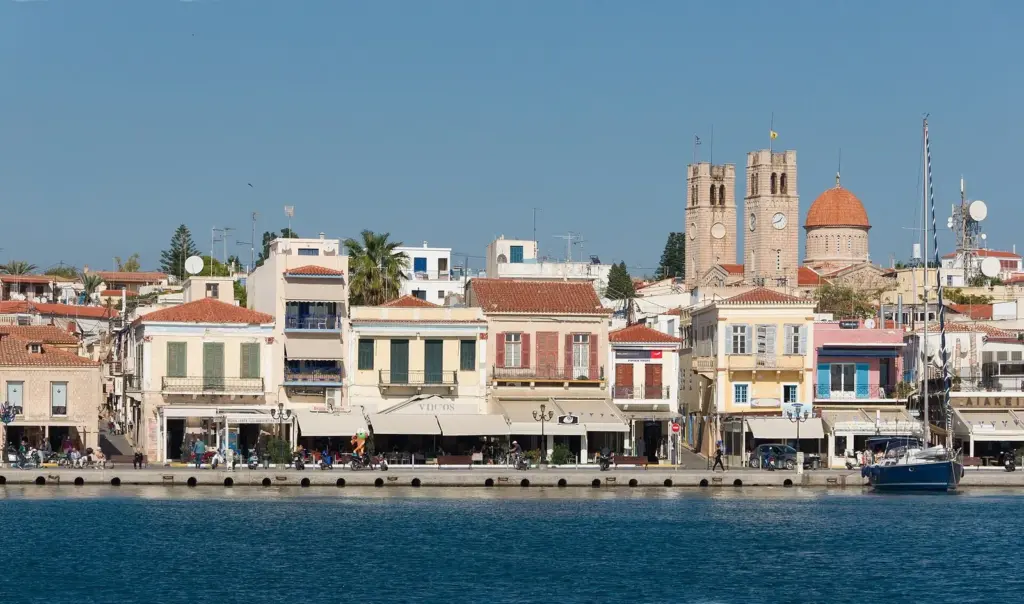 Aegina town waterfront with cafés, moored boats and the cathedral towers behind