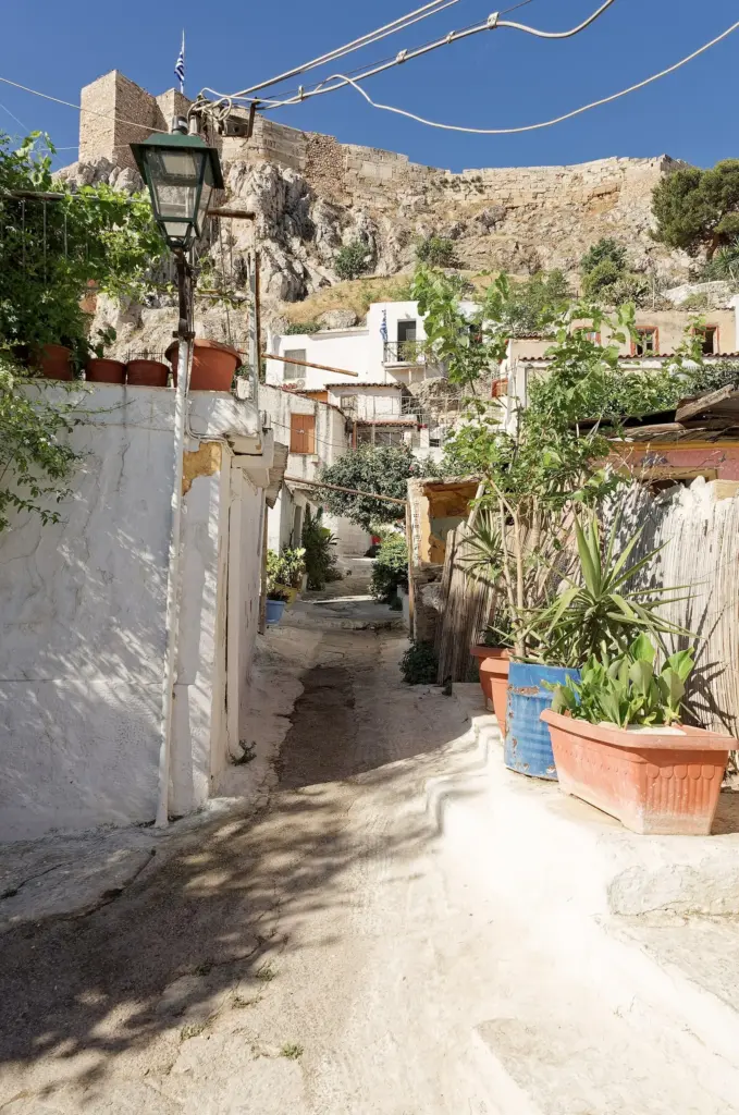 A whitewashed lane of Anafiotika with potted plants, climbing towards the Acropolis rock