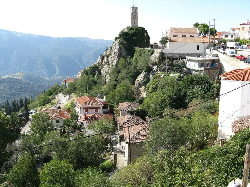Arachova's stone clock tower on a rocky crag above tiled roofs, with mountains behind