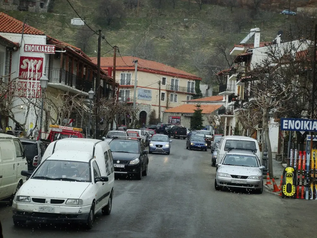 Ski-hire shop signs and parked cars along the main street of Arachova on a grey day