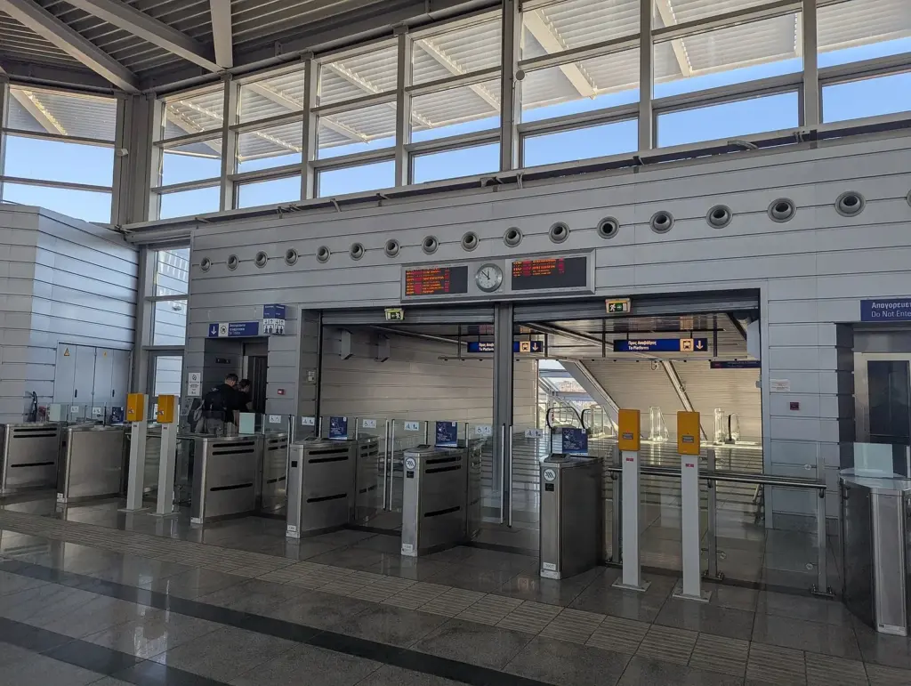 Ticket gates, a glass entrance and departure screens inside the Athens International Airport metro station