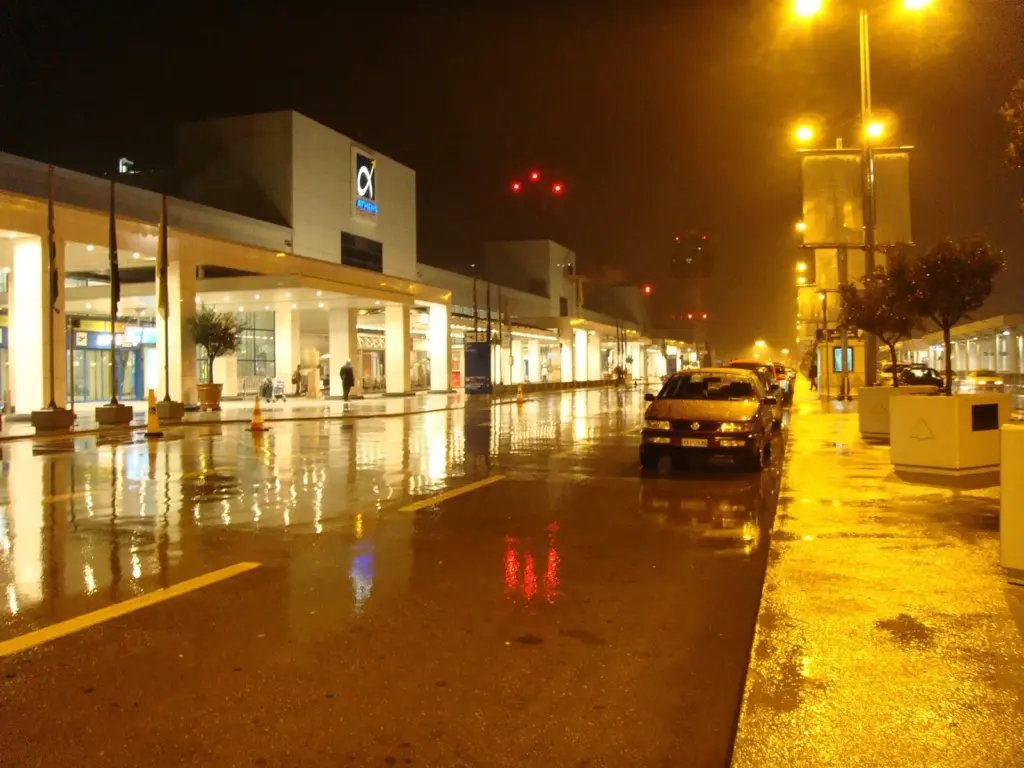 The Athens International Airport terminal forecourt lit up at night after rain