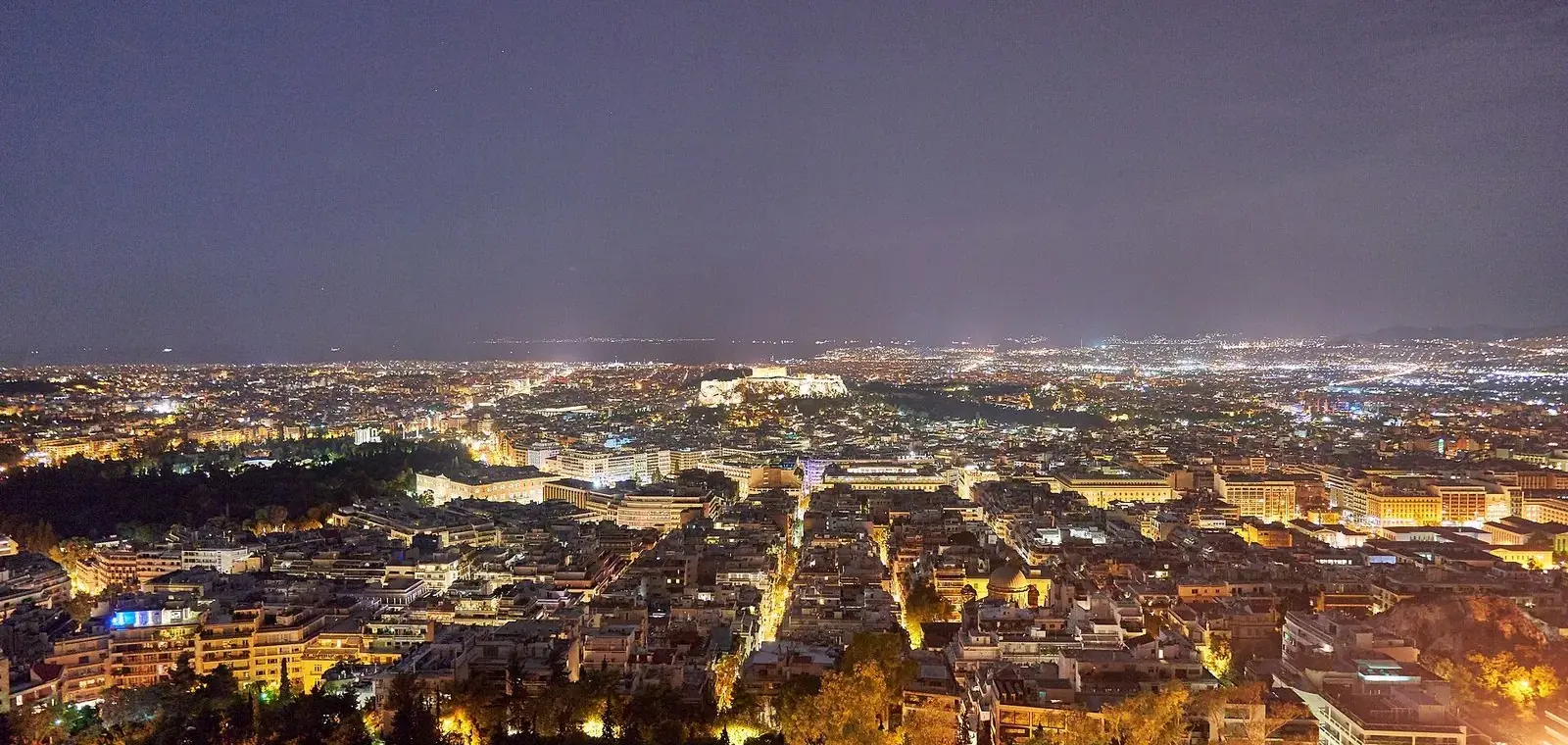 Central Athens lit up at night from Mount Lycabettus, with the floodlit Acropolis in the middle distance