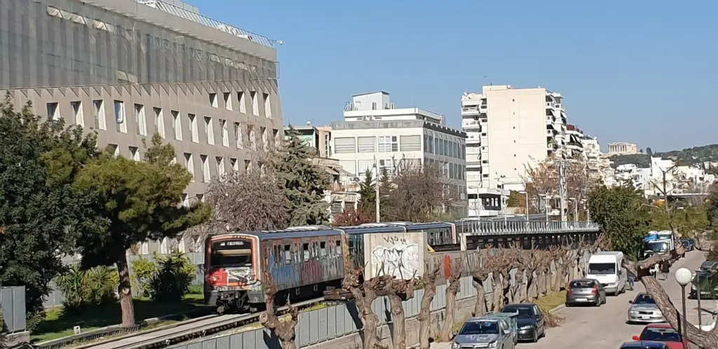 A Line 1 metro train running in an open cutting beside a street in Kallithea