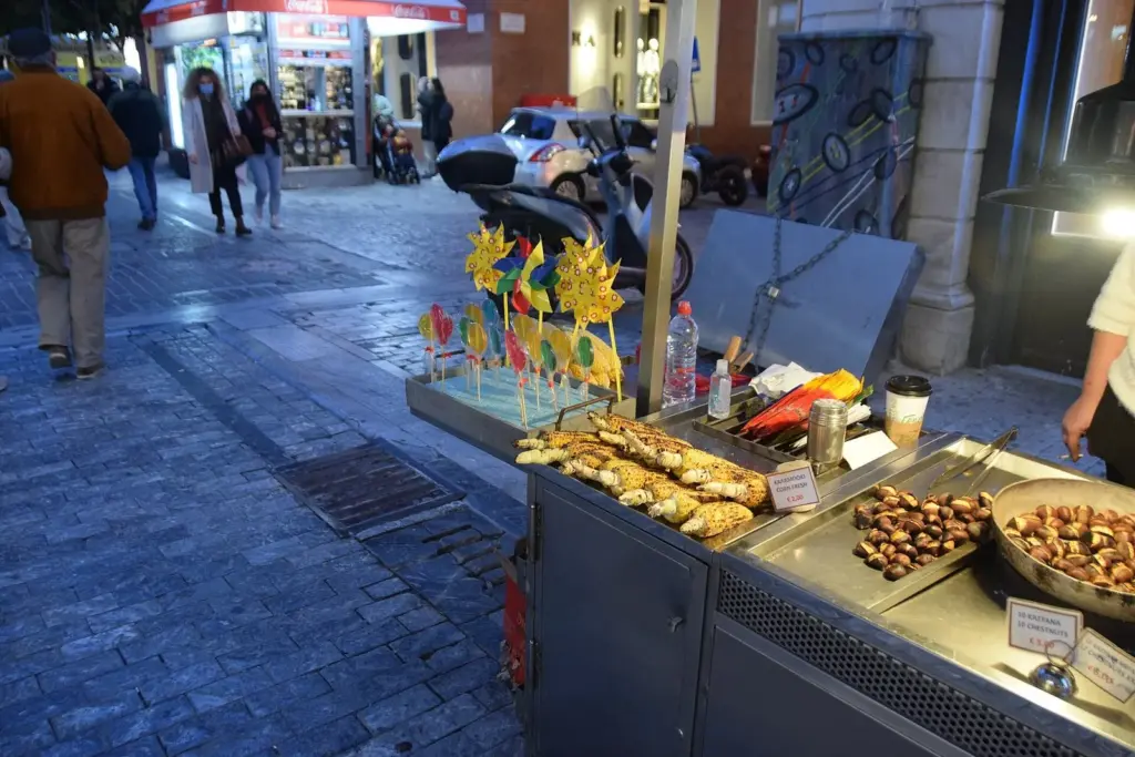 Street vendor's cart with roasting chestnuts and grilled corn cobs on an Athens pavement at dusk