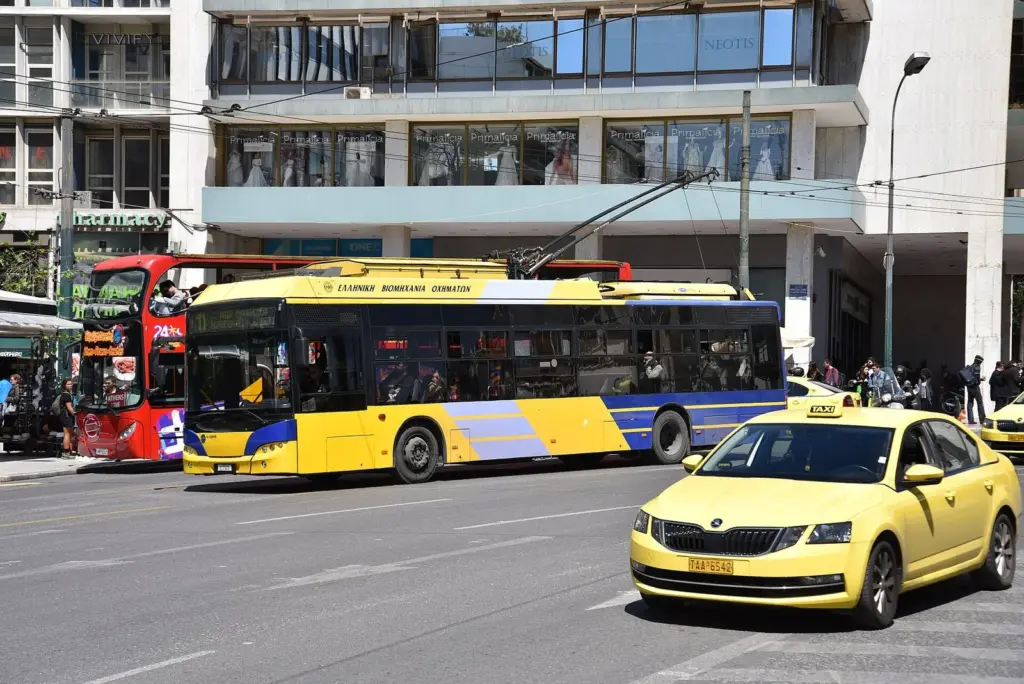 Yellow and blue Athens trolleybus and a yellow taxi on the road beside Syntagma Square