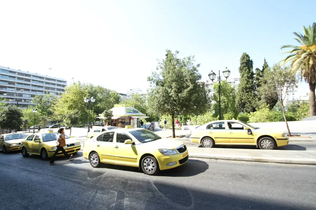Yellow Athens taxis on a sunny street beside trees and palms, with a pedestrian crossing in front of them