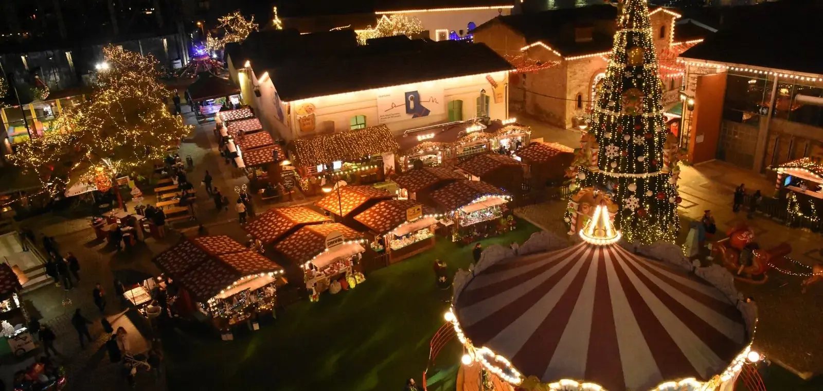 Christmas market stalls, a lit tree and a carousel at the Christmas Factory in Technopolis, Athens