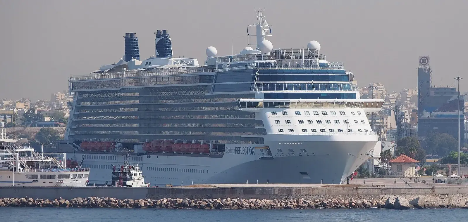 A large cruise ship moored at a Piraeus cruise berth, with Piraeus town behind