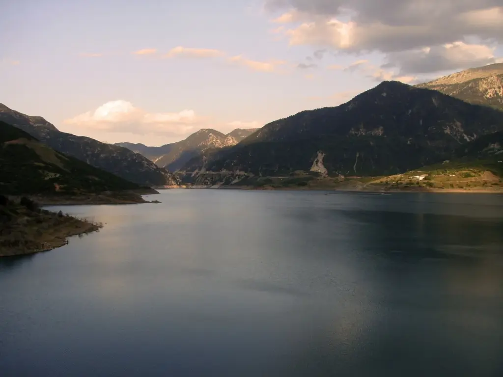 The Evinos reservoir between steep green mountains in western Greece under a pale evening sky