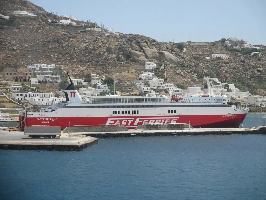 Red-and-white Fast Ferries Andros ship moored at an island quay below a hillside village