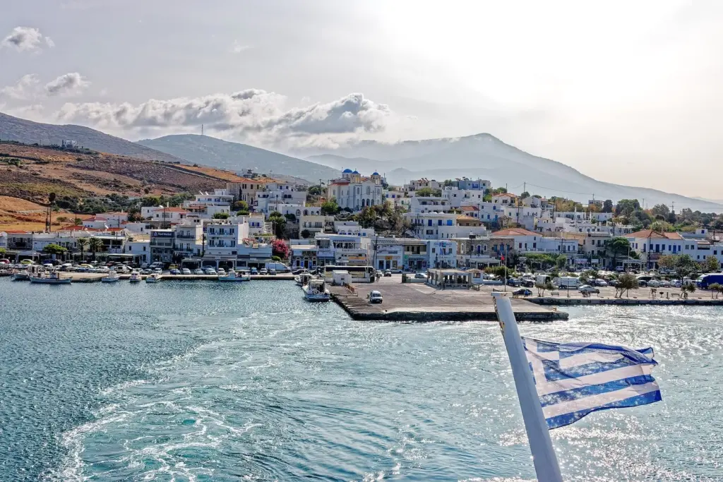 Gavrio harbour on Andros seen from the stern of a ferry, with a Greek flag and the ship's wake in front