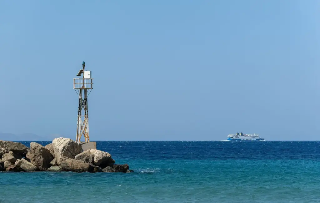 Navigation beacon on a rocky breakwater at Tinos with a Golden Star Ferries ship on the horizon