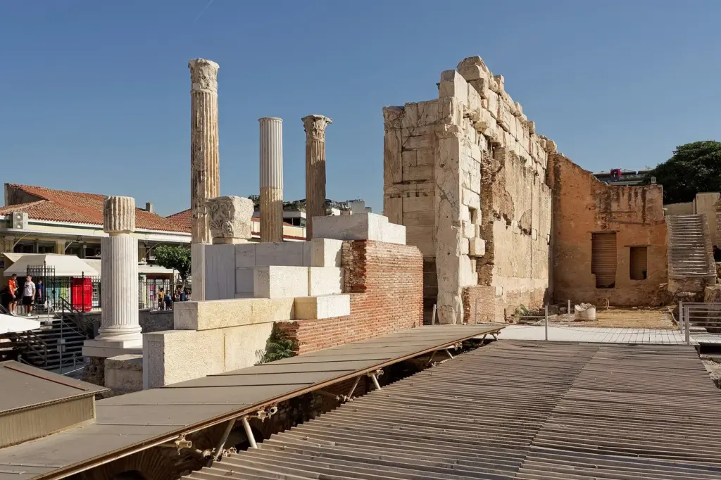 Standing marble columns and the high stone wall of Hadrian's Library beside a wooden visitor walkway