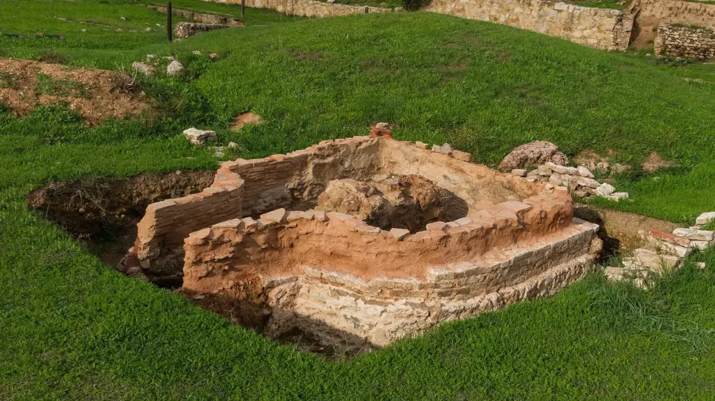 A rectangular brick and stone grave enclosure sunk into green grass in the Kerameikos cemetery