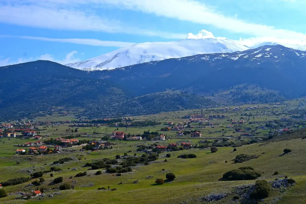 The green Livadi plateau with scattered houses below snow-capped Parnassos peaks