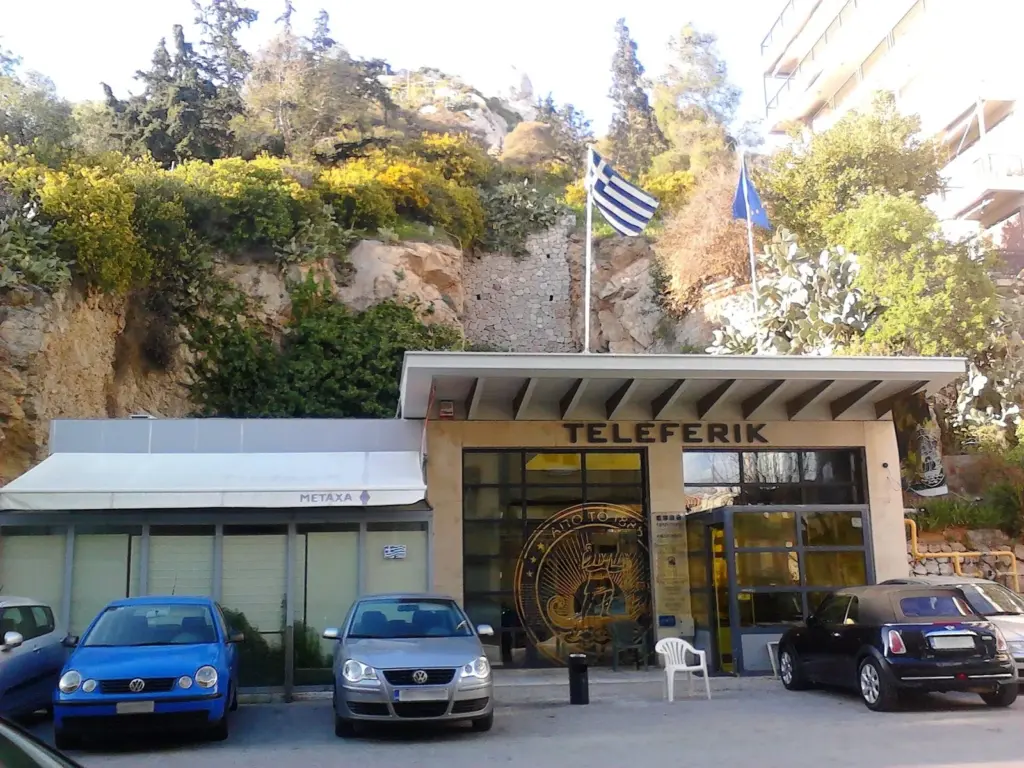 The lower station of the Lycabettus funicular, a low building signed TELEFERIK below pine trees and rock