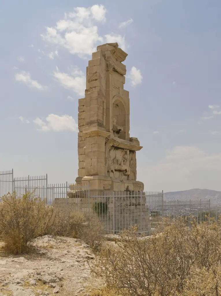 The marble Philopappos Monument on the summit of the Hill of the Muses behind a metal railing