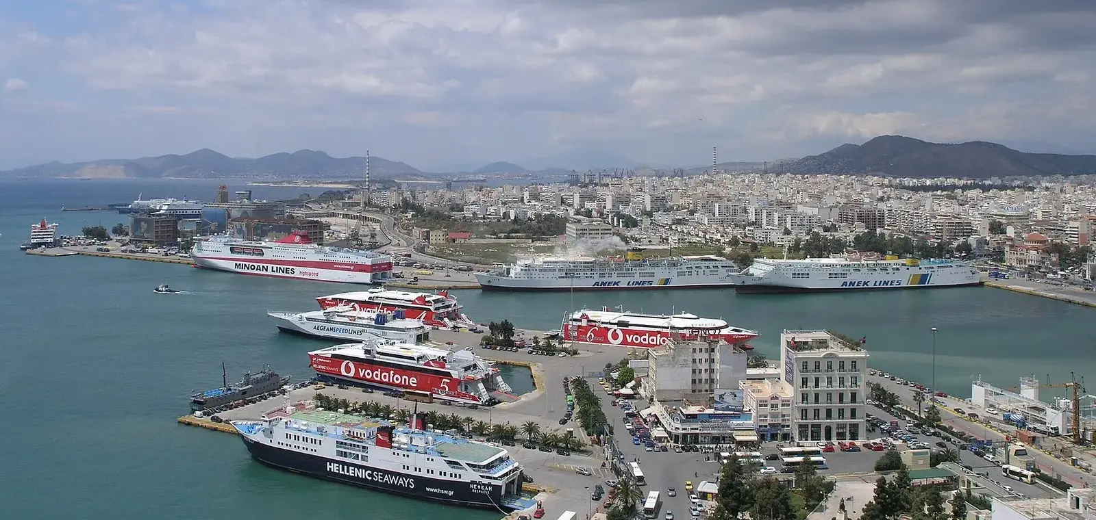 Aerial view of Piraeus port's central harbour, with ferries berthed along the quays and the city and hills behind