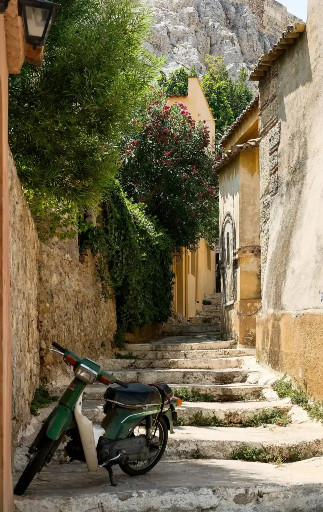 Stepped lane in Plaka with old walls, flowering plants and a parked scooter