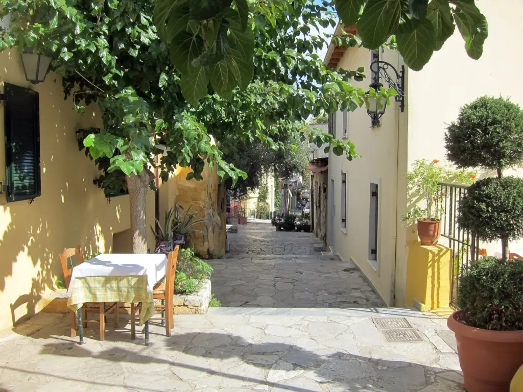 A single taverna table laid under a tree in a stone-paved lane on Thespidos Street, Plaka