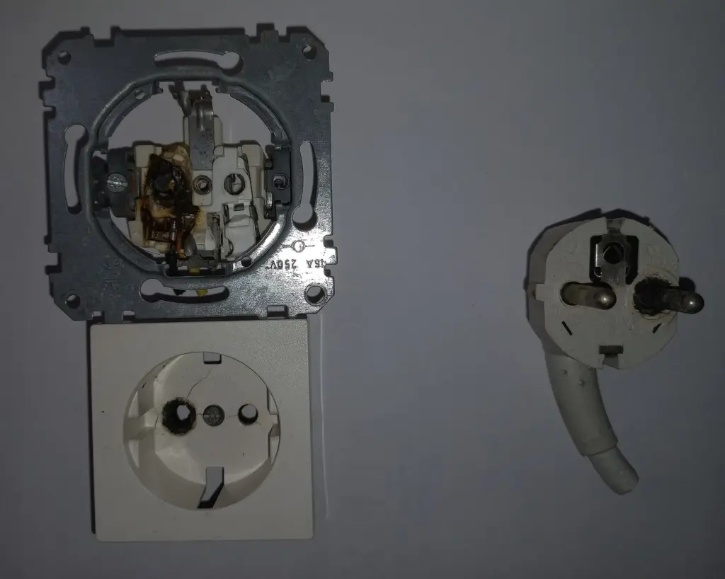 Scorched Type F socket insert beside a matching plug, removed from the wall after overheating
