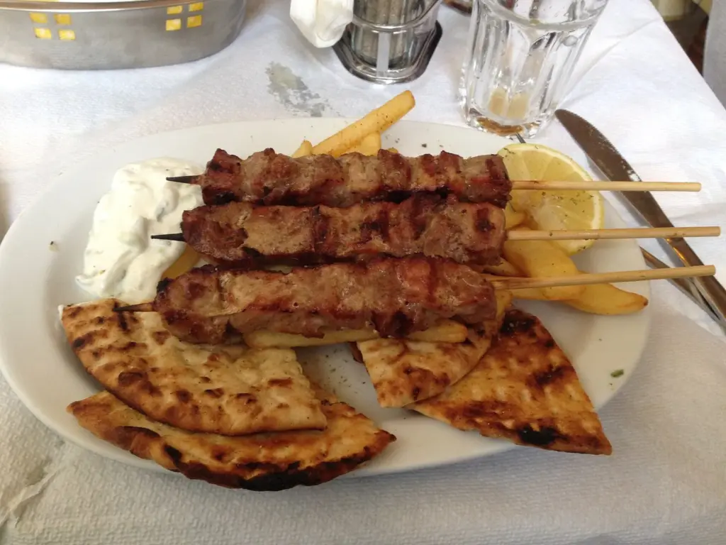 Grilled meat skewers with pitta, chips and tzatziki on a paper tablecloth