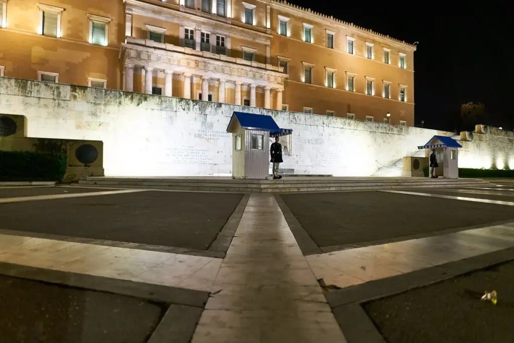 The Tomb of the Unknown Soldier and its sentry boxes floodlit at night below the Hellenic Parliament