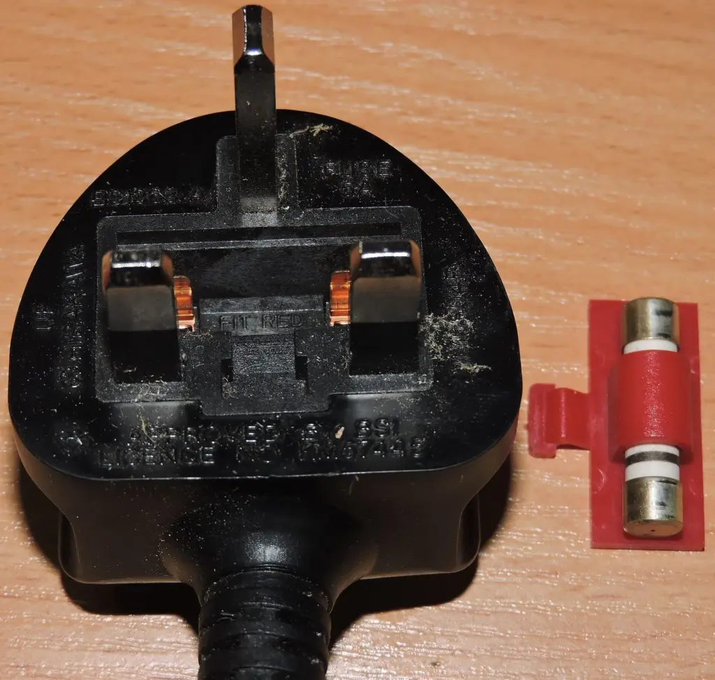 Underside of a UK three-pin plug with its cartridge fuse removed and lying beside it