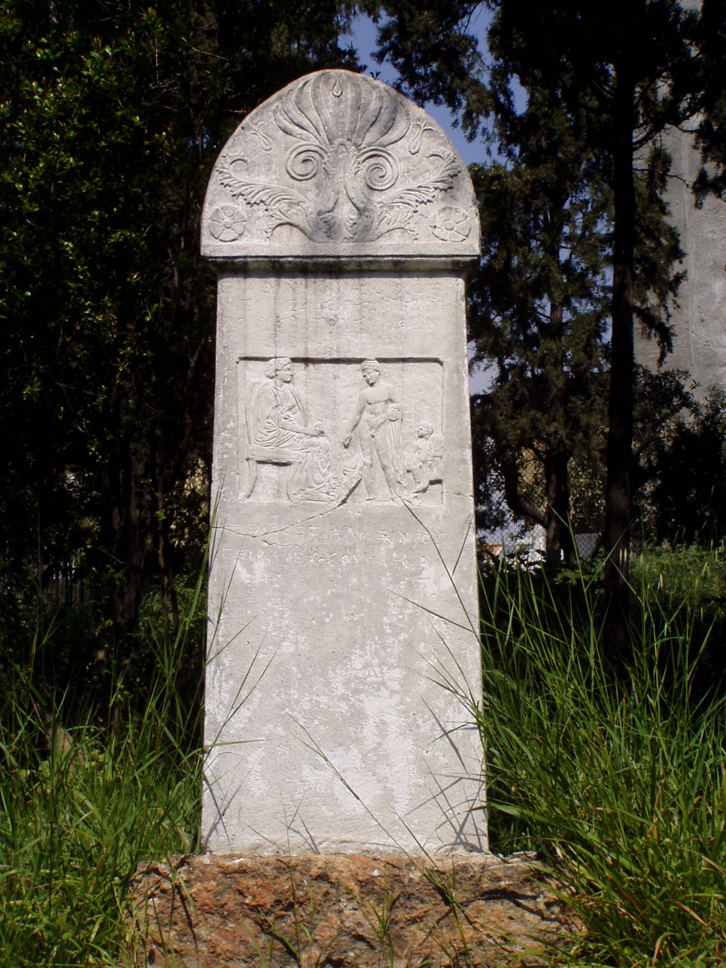 A carved marble grave stele at Kerameikos in Athens has a floral crown and a relief of human figures.