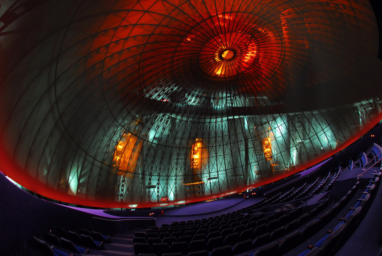 Fisheye view inside the Eugenides Foundation planetarium in Athens, showing the lit ribbed dome above curving rows of blue seats.