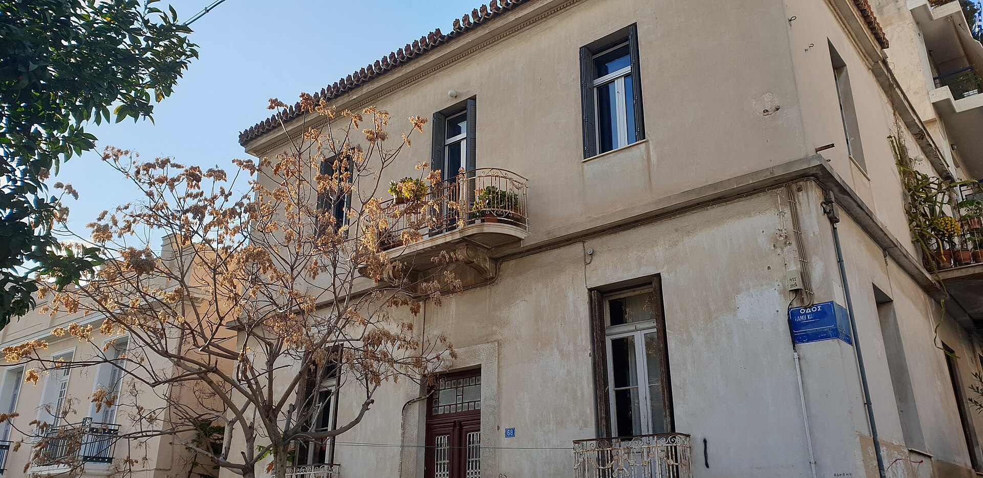 An older corner house with iron balconies and street trees stands in Koukaki below Filopappou Hill, Athens.