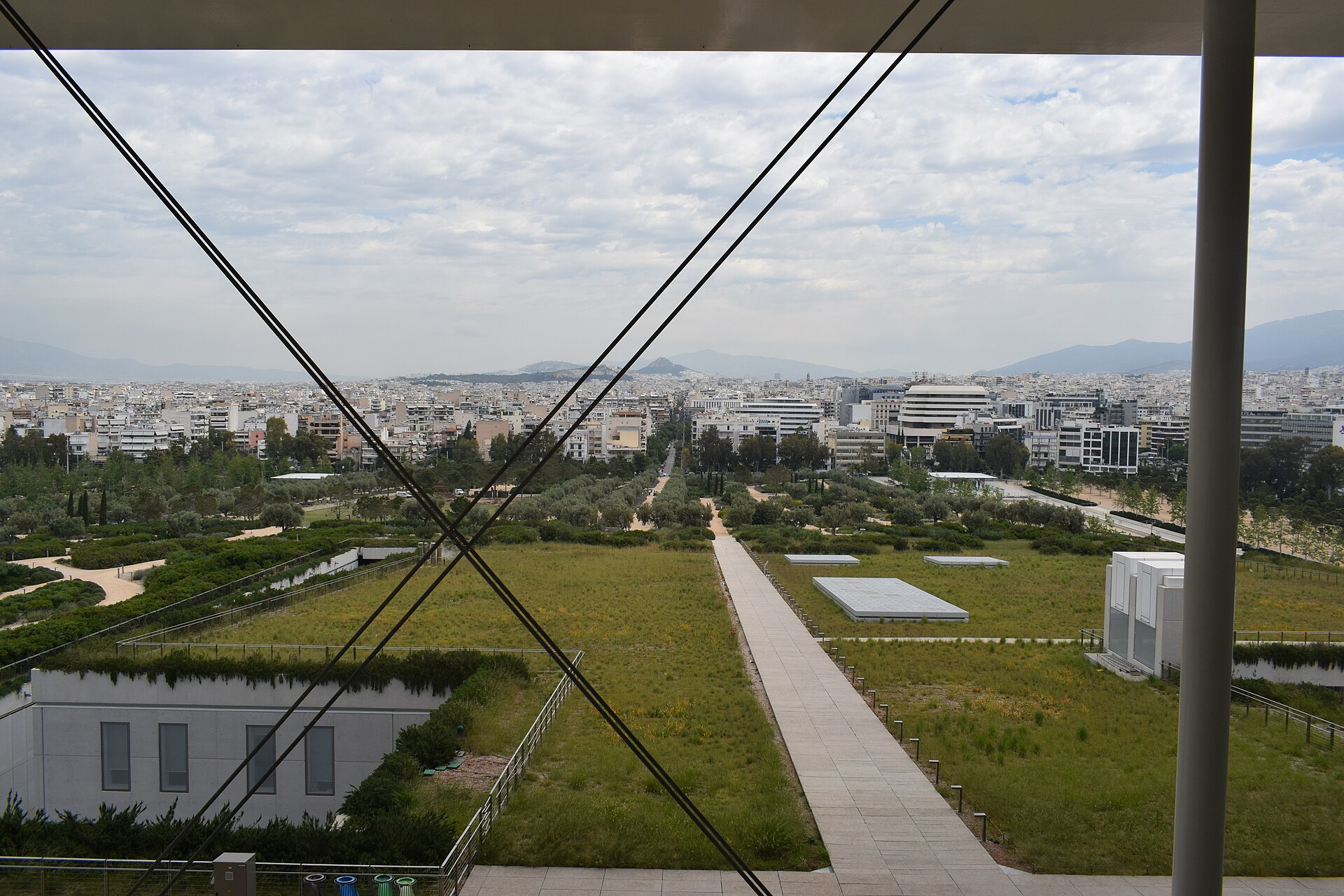 The SNFCC park stretches beyond the canopy supports, with planted roofs, walking paths and the Athens skyline behind.